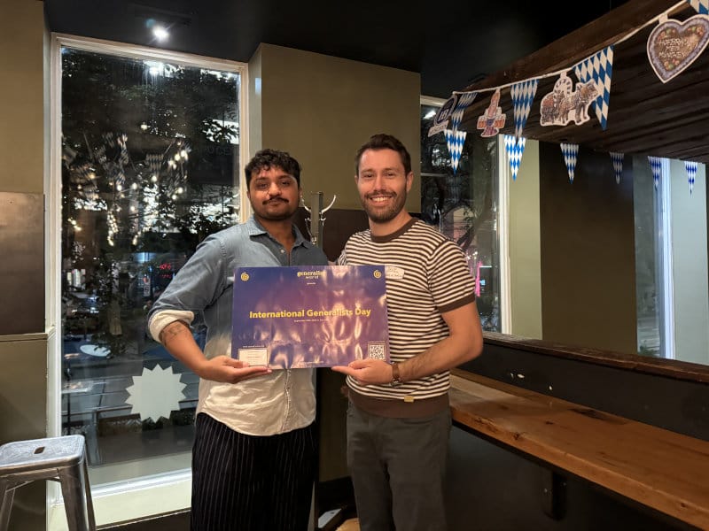 Two meetup hosts holding an International Generalist Day poster at their venue