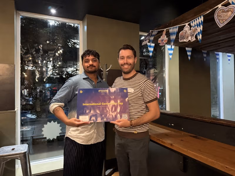 Two meetup hosts holding an International Generalist Day poster at their venue