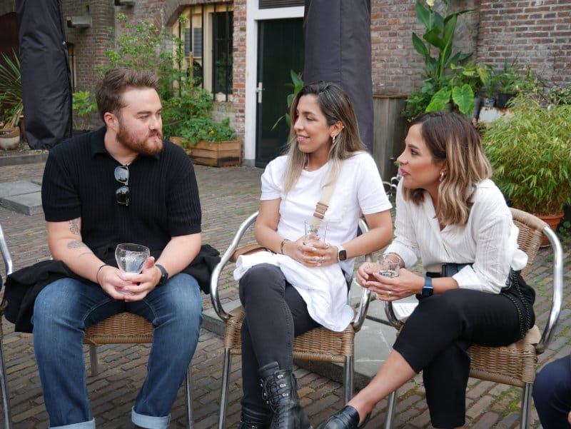 Three generalists sitting outside in a courtyard with drinks, mid-conversation