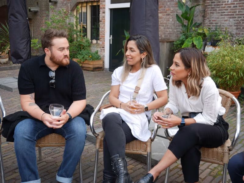 Three generalists sitting outside in a courtyard with drinks, mid-conversation
