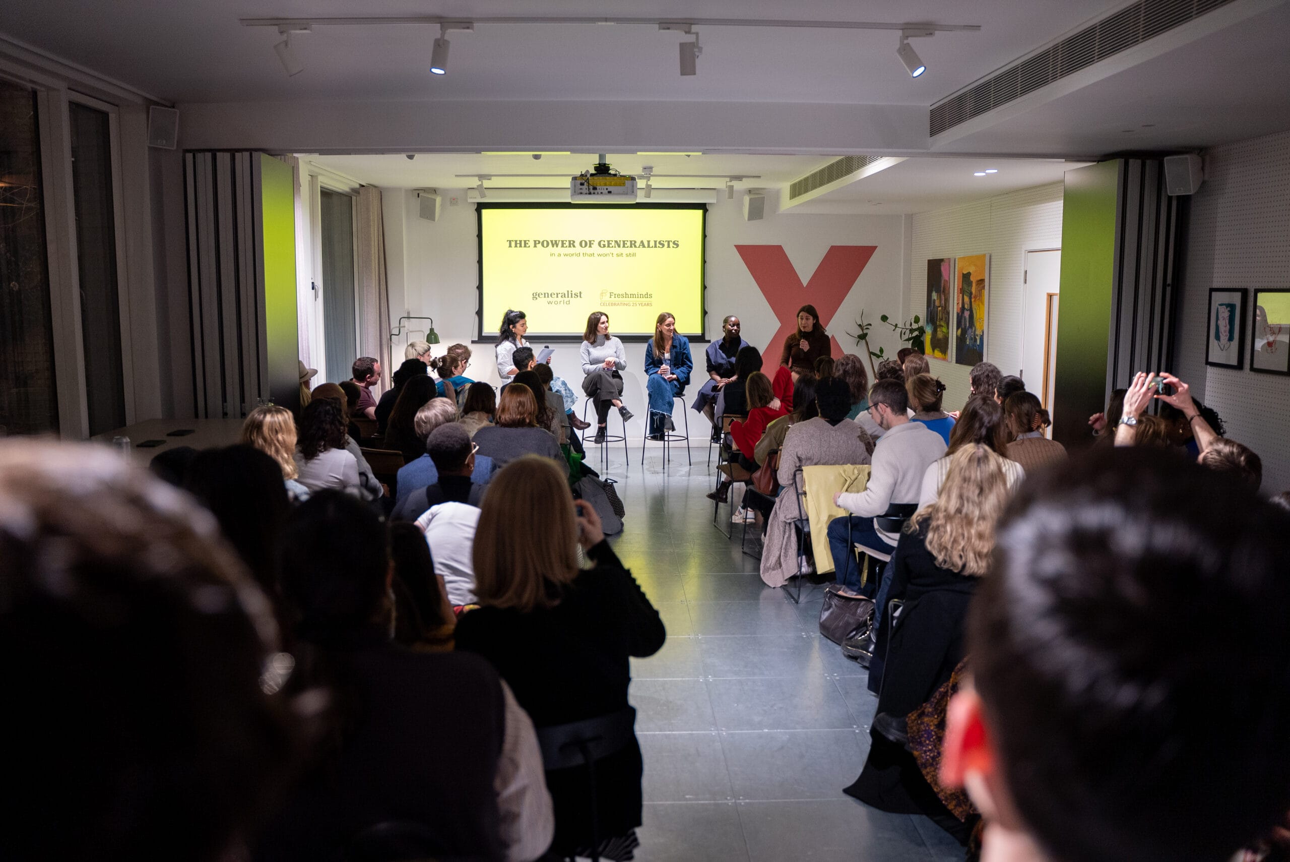 A packed audience watching a panel discussion titled The Power of Generalists